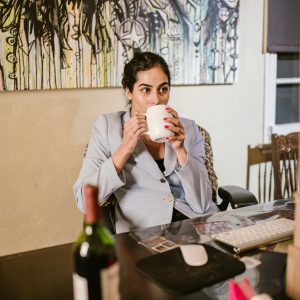 Businesswoman enjoying coffee at her home office desk amidst remote work setup.