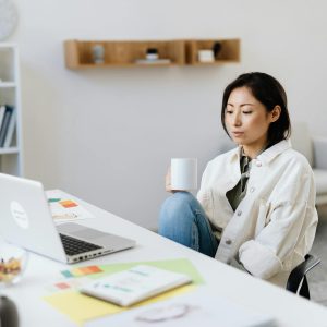 Businesswoman in a modern office setting working on a laptop with a coffee cup.