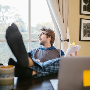 Man enjoying a relaxed home office setup with feet up, looking out the window.